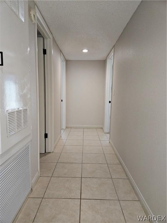 hall with baseboards, a textured ceiling, and light tile patterned flooring