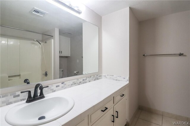 bathroom featuring tile patterned floors, vanity, baseboards, visible vents, and decorative backsplash