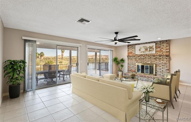 living area with light tile patterned floors, visible vents, a brick fireplace, ceiling fan, and a textured ceiling