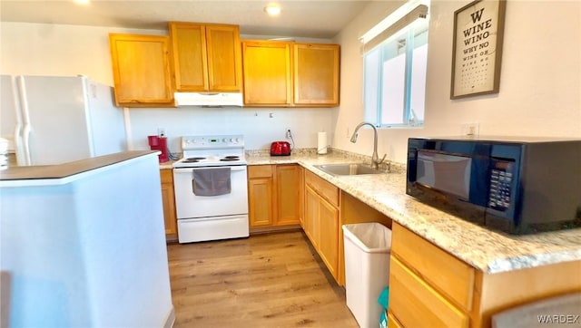 kitchen featuring light wood finished floors, a sink, light stone countertops, white appliances, and under cabinet range hood