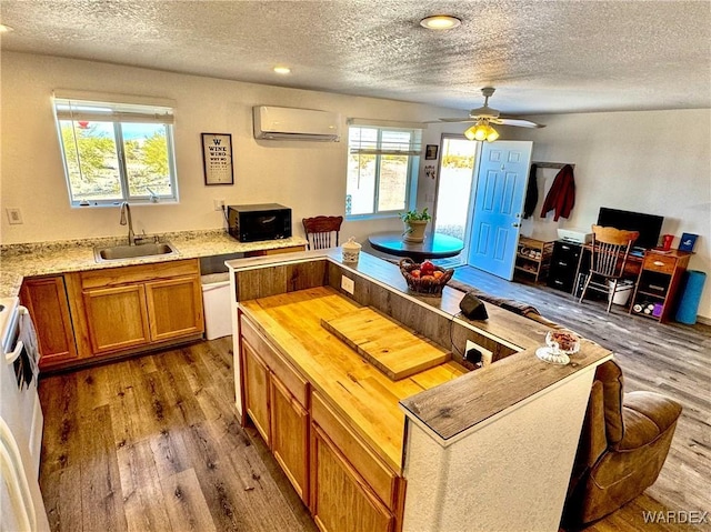 kitchen featuring wood finished floors, a wall mounted air conditioner, black microwave, wooden counters, and a sink