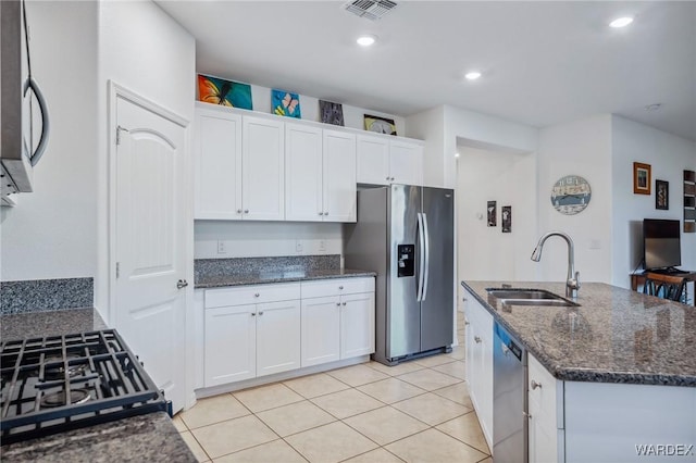 kitchen featuring stainless steel appliances, visible vents, white cabinets, a sink, and dark stone countertops