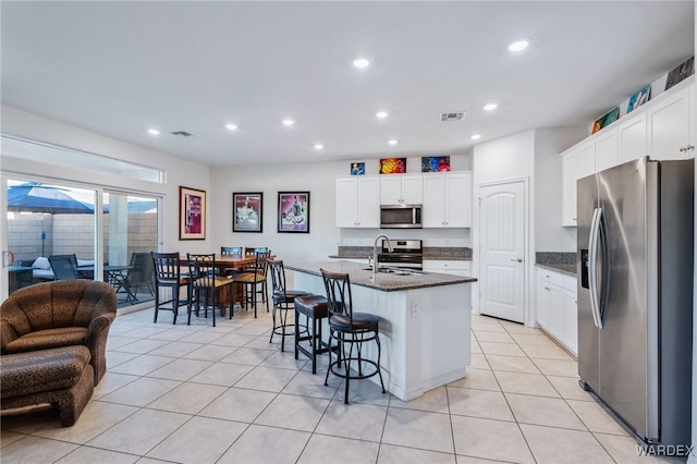 kitchen with stainless steel appliances, visible vents, an island with sink, and white cabinetry