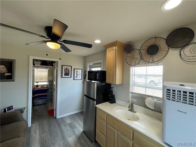 kitchen with light countertops, freestanding refrigerator, light brown cabinets, a sink, and black microwave