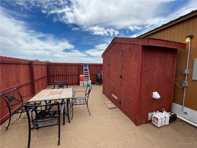 view of patio featuring a storage shed, a fenced backyard, an outdoor structure, and outdoor dining space