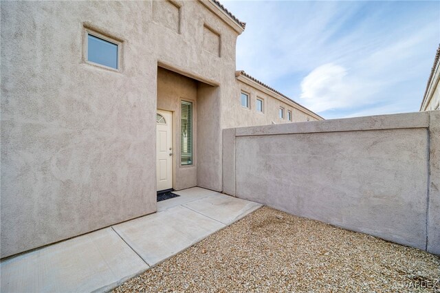 property entrance with a patio area, fence, a tile roof, and stucco siding