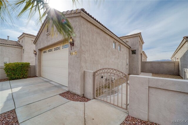 view of home's exterior with driveway, a tiled roof, an attached garage, fence, and stucco siding