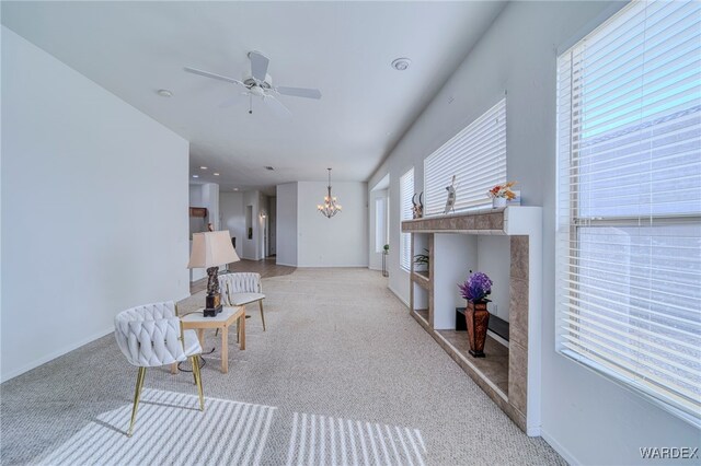 sitting room featuring baseboards, ceiling fan with notable chandelier, and light colored carpet