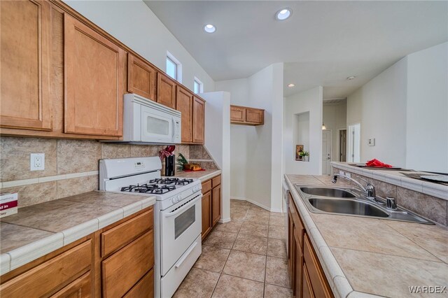 kitchen with brown cabinets, tile countertops, backsplash, a sink, and white appliances