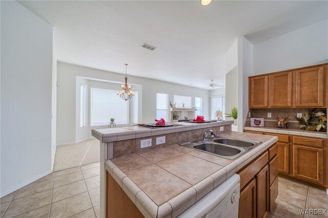 kitchen featuring tile countertops, a sink, visible vents, brown cabinets, and a center island with sink