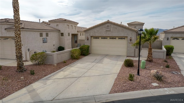 mediterranean / spanish house with a tile roof, stucco siding, concrete driveway, an attached garage, and fence