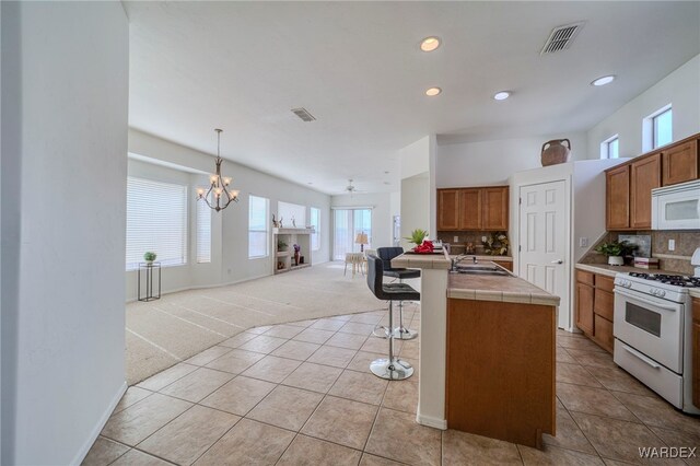 kitchen featuring white appliances, visible vents, brown cabinets, an island with sink, and pendant lighting