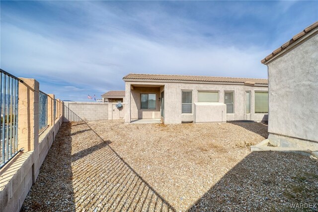 back of house with a fenced backyard, a tile roof, and stucco siding