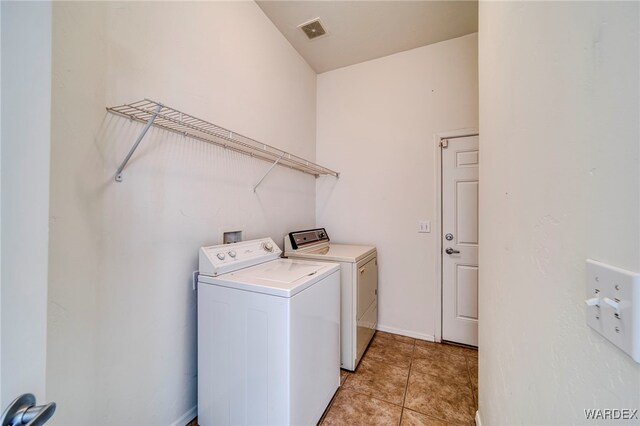 clothes washing area featuring washer and clothes dryer, visible vents, light tile patterned flooring, laundry area, and baseboards