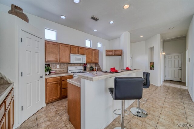 kitchen featuring an island with sink, white appliances, visible vents, and brown cabinets