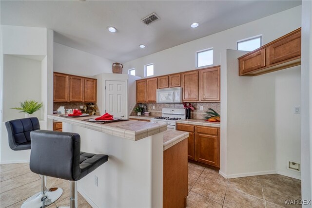 kitchen with tile countertops, white appliances, visible vents, brown cabinetry, and a kitchen bar