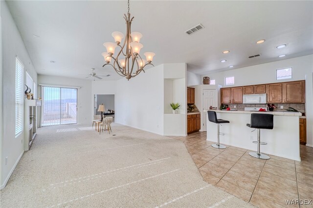 kitchen with brown cabinets, light countertops, visible vents, hanging light fixtures, and white microwave