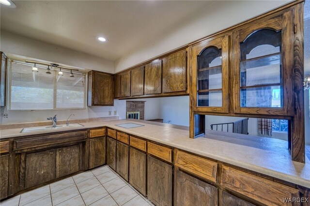 kitchen featuring light tile patterned floors, light countertops, glass insert cabinets, a sink, and a peninsula