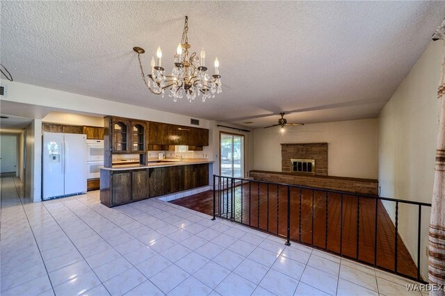 kitchen featuring dark brown cabinetry, white appliances, open floor plan, a brick fireplace, and pendant lighting