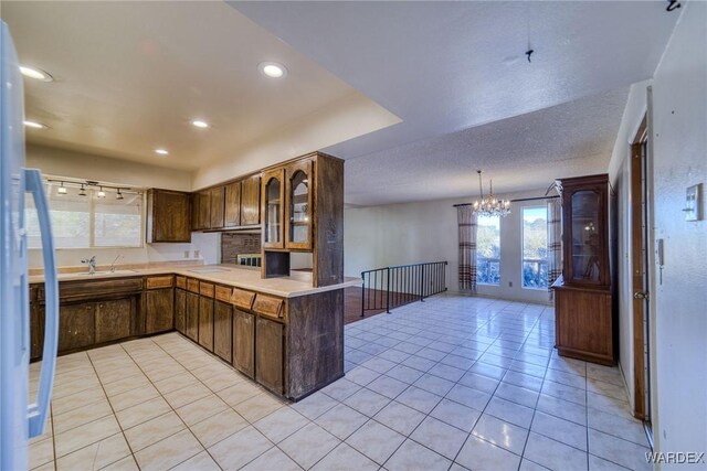 kitchen with light tile patterned flooring, a peninsula, a sink, light countertops, and glass insert cabinets