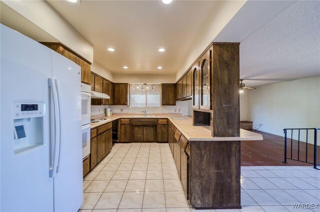 kitchen featuring a peninsula, white appliances, light tile patterned floors, and light countertops