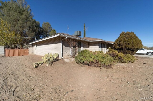 view of front of home featuring cooling unit, brick siding, and fence