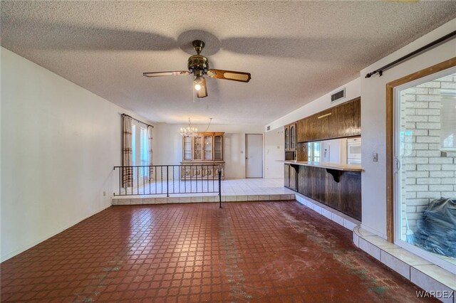 unfurnished living room with a healthy amount of sunlight, visible vents, a textured ceiling, and ceiling fan with notable chandelier