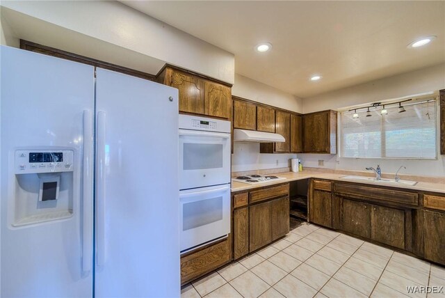 kitchen featuring light tile patterned floors, under cabinet range hood, white appliances, a sink, and light countertops