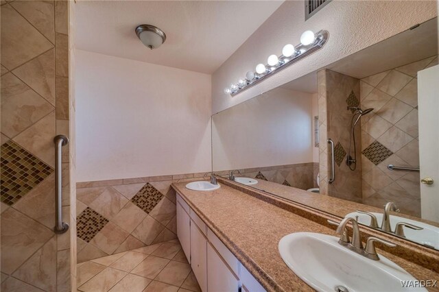 bathroom with double vanity, visible vents, tile walls, and a sink