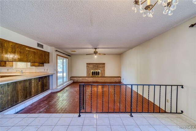 kitchen featuring light tile patterned floors, ceiling fan with notable chandelier, visible vents, light countertops, and a glass covered fireplace