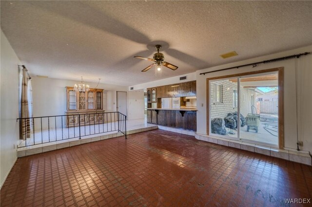 unfurnished living room featuring ceiling fan with notable chandelier, a textured ceiling, and visible vents