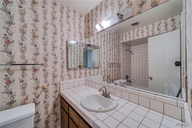 full bathroom with visible vents, toilet, vanity,  shower combination, and wallpapered walls