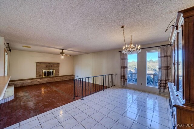 empty room with a glass covered fireplace, light tile patterned flooring, a textured ceiling, and ceiling fan with notable chandelier