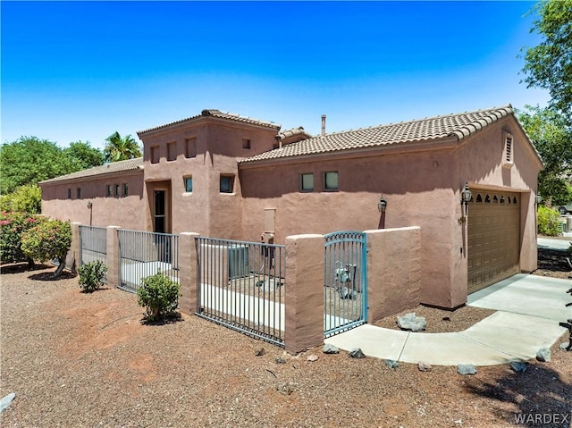 view of front of property with a tile roof, a fenced front yard, an attached garage, a gate, and stucco siding