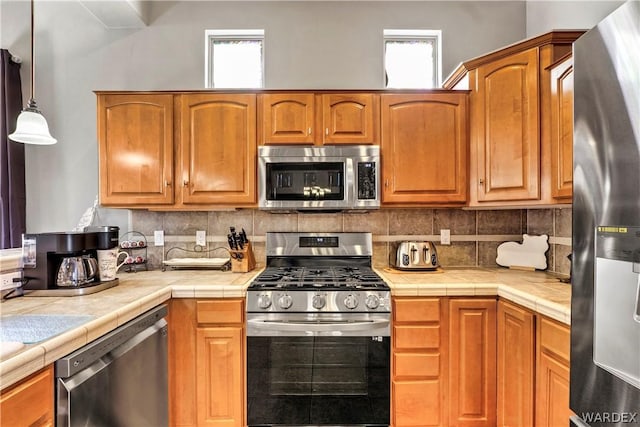 kitchen featuring appliances with stainless steel finishes, tile counters, brown cabinetry, and decorative backsplash