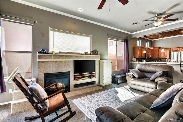 carpeted living area with ornamental molding, visible vents, a fireplace, and a ceiling fan