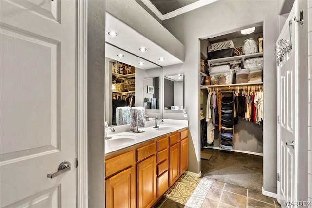 full bath with double vanity, crown molding, a walk in closet, and a sink