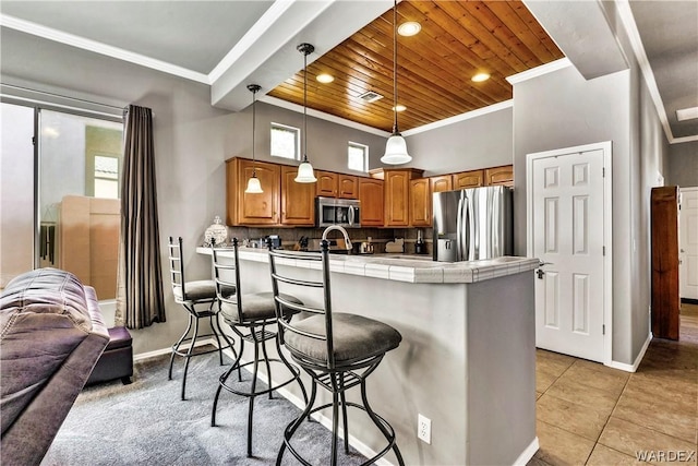 kitchen featuring stainless steel appliances, brown cabinetry, crown molding, and tile countertops