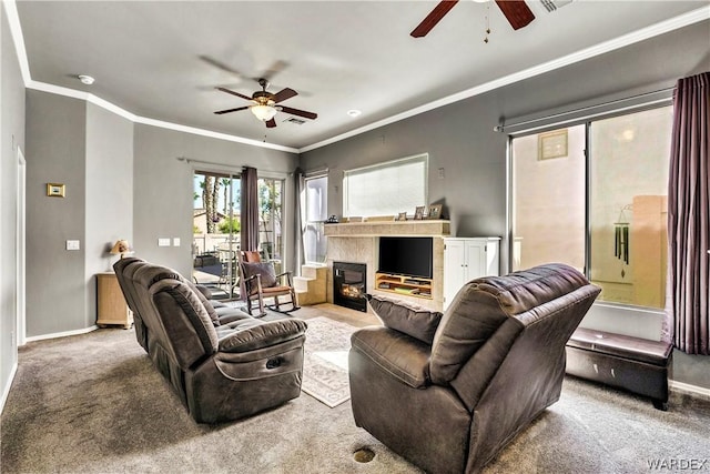 carpeted living area featuring crown molding, a glass covered fireplace, a ceiling fan, and baseboards