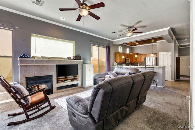 living room featuring crown molding, a tile fireplace, visible vents, and light colored carpet