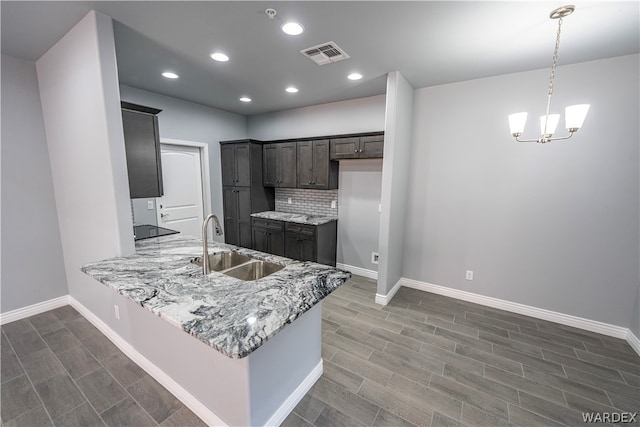 kitchen with a peninsula, a sink, visible vents, baseboards, and decorative backsplash