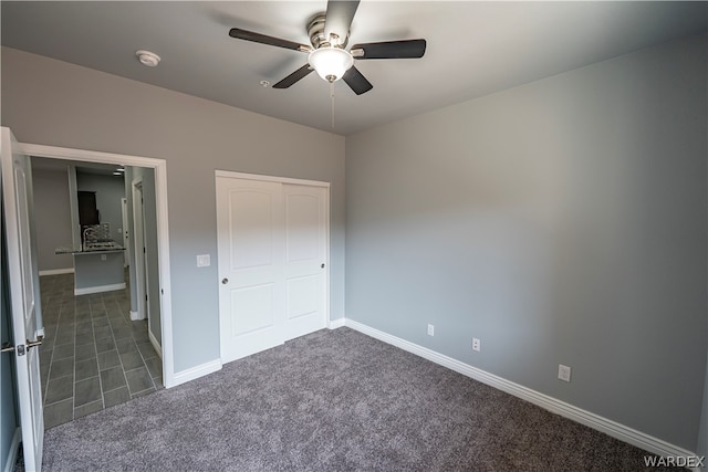 unfurnished bedroom featuring dark colored carpet, a closet, a ceiling fan, and baseboards