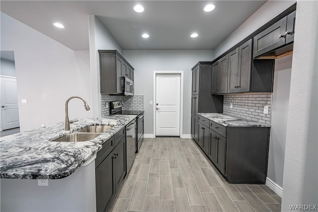 kitchen featuring wood tiled floor, appliances with stainless steel finishes, light stone counters, and a sink