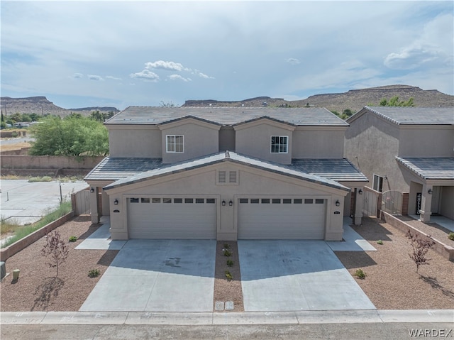 view of front facade with driveway, a mountain view, fence, and stucco siding