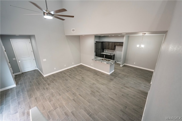 unfurnished living room featuring baseboards, visible vents, dark wood-style flooring, and ceiling fan with notable chandelier