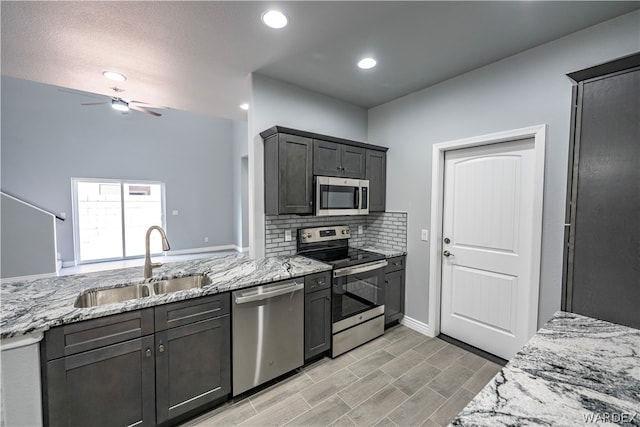 kitchen featuring light stone counters, tasteful backsplash, appliances with stainless steel finishes, a sink, and ceiling fan