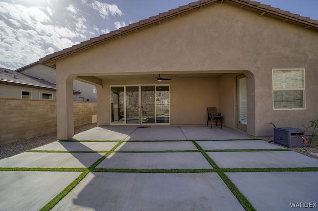 rear view of property with stucco siding, a patio area, ceiling fan, fence, and a tiled roof