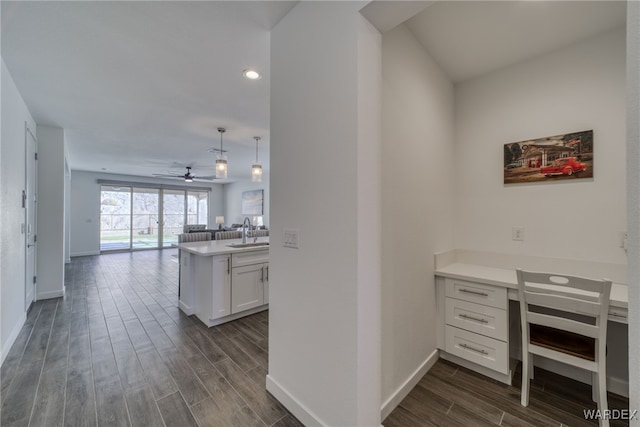 interior space featuring built in desk, open floor plan, wood finish floors, white cabinetry, and a sink