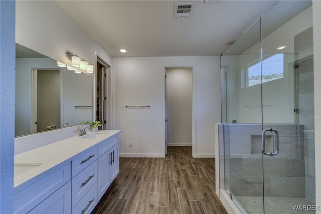 full bathroom featuring a sink, wood finished floors, baseboards, visible vents, and a shower stall