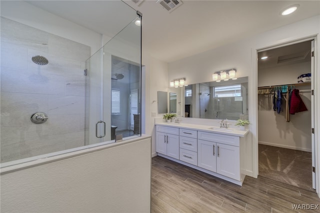 full bathroom featuring double vanity, visible vents, wood finish floors, a shower stall, and a sink